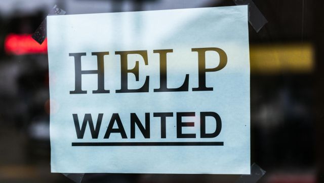 Close-up of a Help Wanted sign taped to a glass window in a storefront.