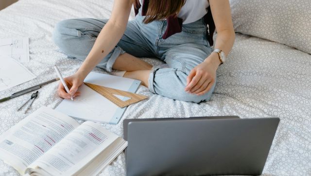Teen girl engaged in online learning while sitting on her bed, using a laptop and taking notes.